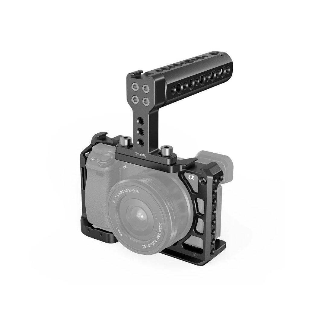 SmallRig_Handheld_Kit_for_Sony_A6100_A6300_A6400_A6500_3719_001 SmallRig Handheld Kit for Sony A6100/6300/6400/6500 3719, jossa on musta metallinen häkki ja yläkahva, asennetaan peilittömään kameraan ja tarjoaa suojaa ja useita lisävarusteiden kiinnityspisteitä. Kamera ja objektiivi ovat osittain näkyvissä häkin sisällä.