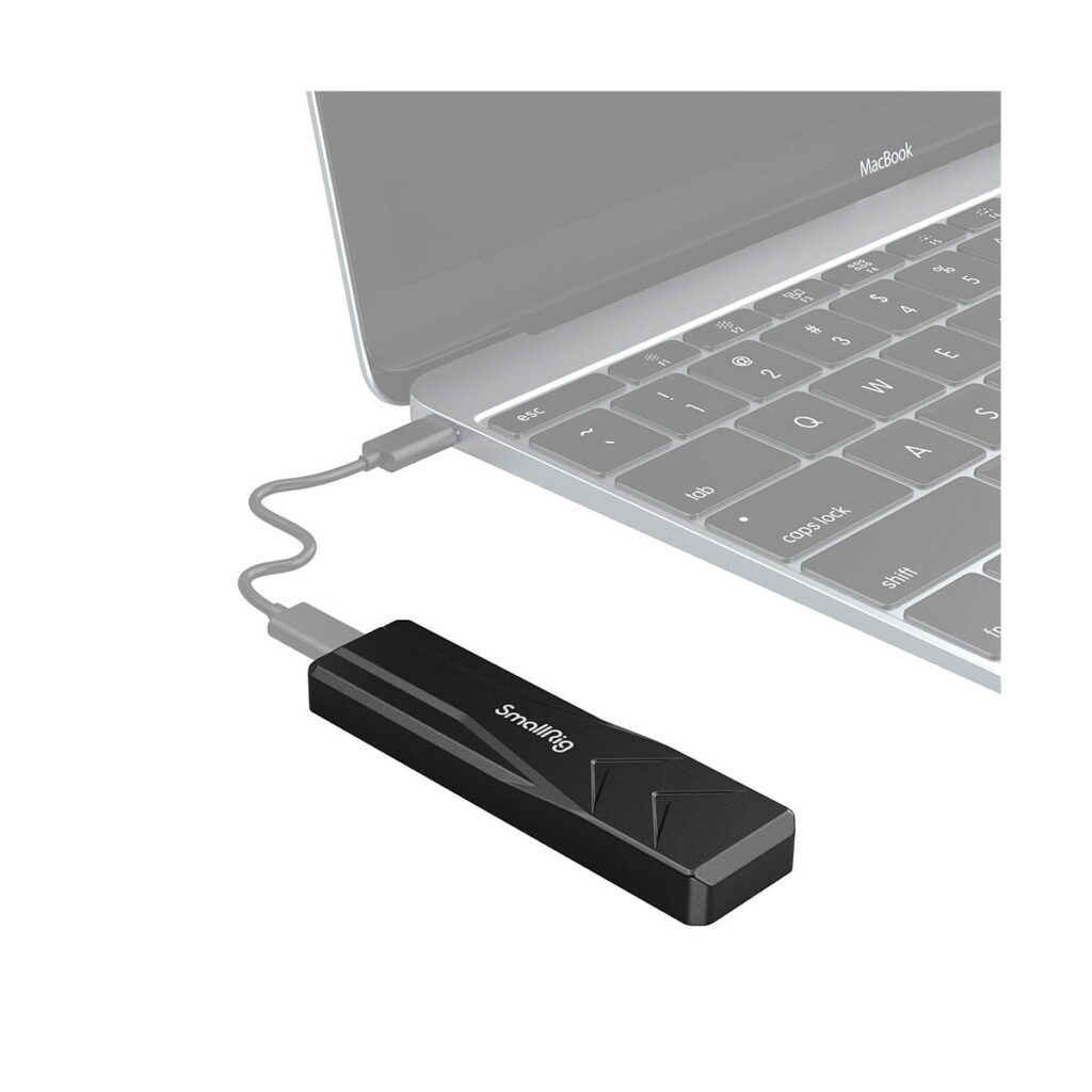 SmallRig_M_2_SSD_Enclosure_SD-01_3479_004 SmallRig 3479 M.2 SSD Enclosure SD-01, musta USB-laite, on liitetty kannettavaan tietokoneeseen lyhyellä USB-kaapelilla, ja kannettavan tietokoneen näppäimistön ja ohjauslevyn osat ovat osittain näkyvissä.