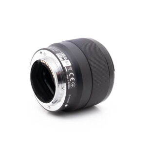 Sony 50mm f18-1 Lähikuva Sony FE 50mm f/1.8 - Käytetty -objektiivista kyljellään, jossa korostuvat metallinen kiinnitys elektronisilla koskettimilla, sertifiointimerkinnät ja piipun kuvioitu ote.