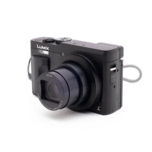 Panasonic DC-TZ90 7657-4 Panasonic Lumix DC-TZ90 - Käytetty digitaalikamera on kuvattu vasemmalle kallistettuna valkoisella taustalla, ja siihen on kiinnitetty osittain laajennettu Leica-zoom-objektiivi ja harmaa rannehihna.