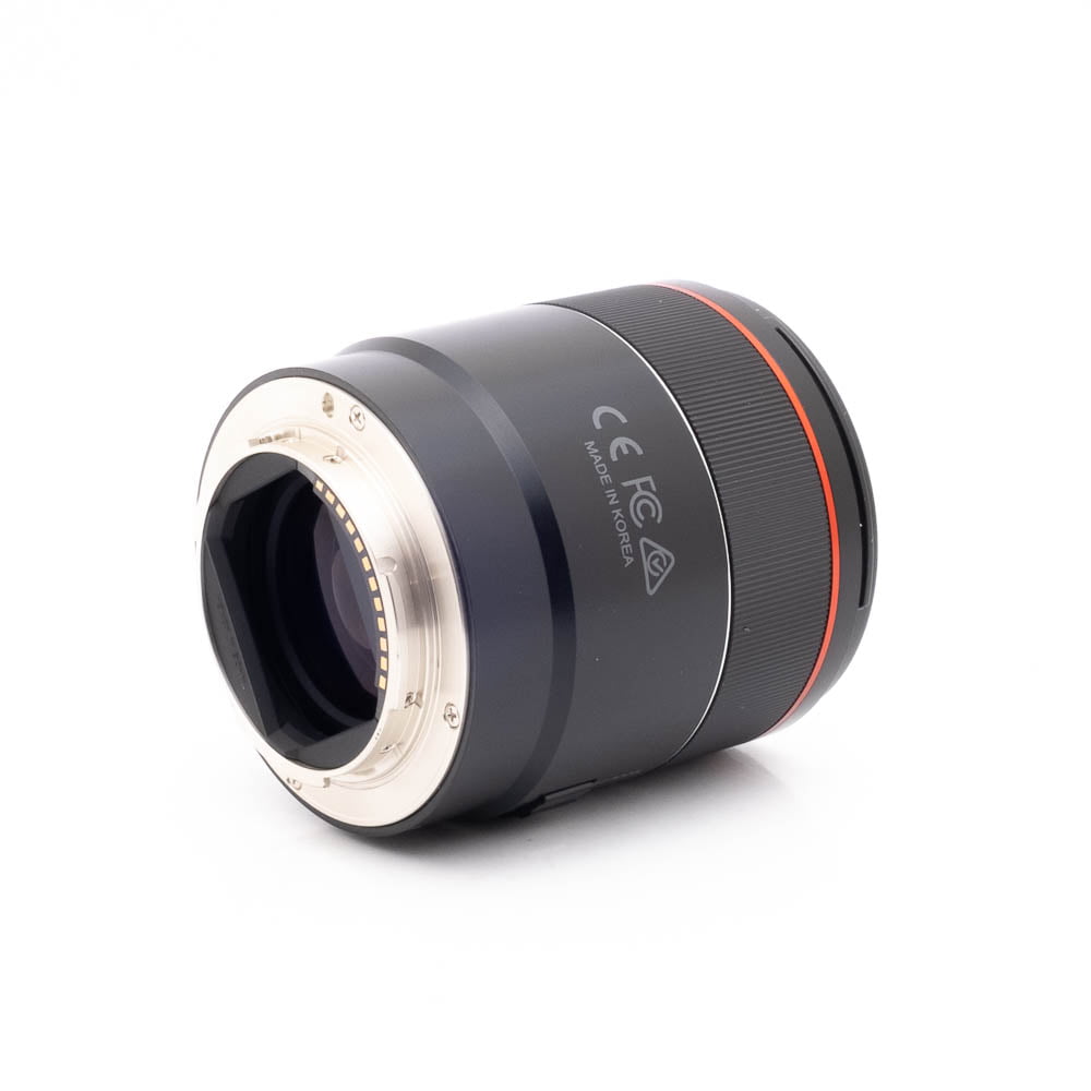 Samyang 75mm f18 FE Canon-1 Panasonic Lumix DC-TZ90 - Käytetty on kuvattu valkoisella pohjalla, ja siinä on musta runko, hopeinen metallirunko ja punainen korostusrengas. Sen kyljessä näkyvät sertifiointimerkinnät ja Made in Korea -teksti.