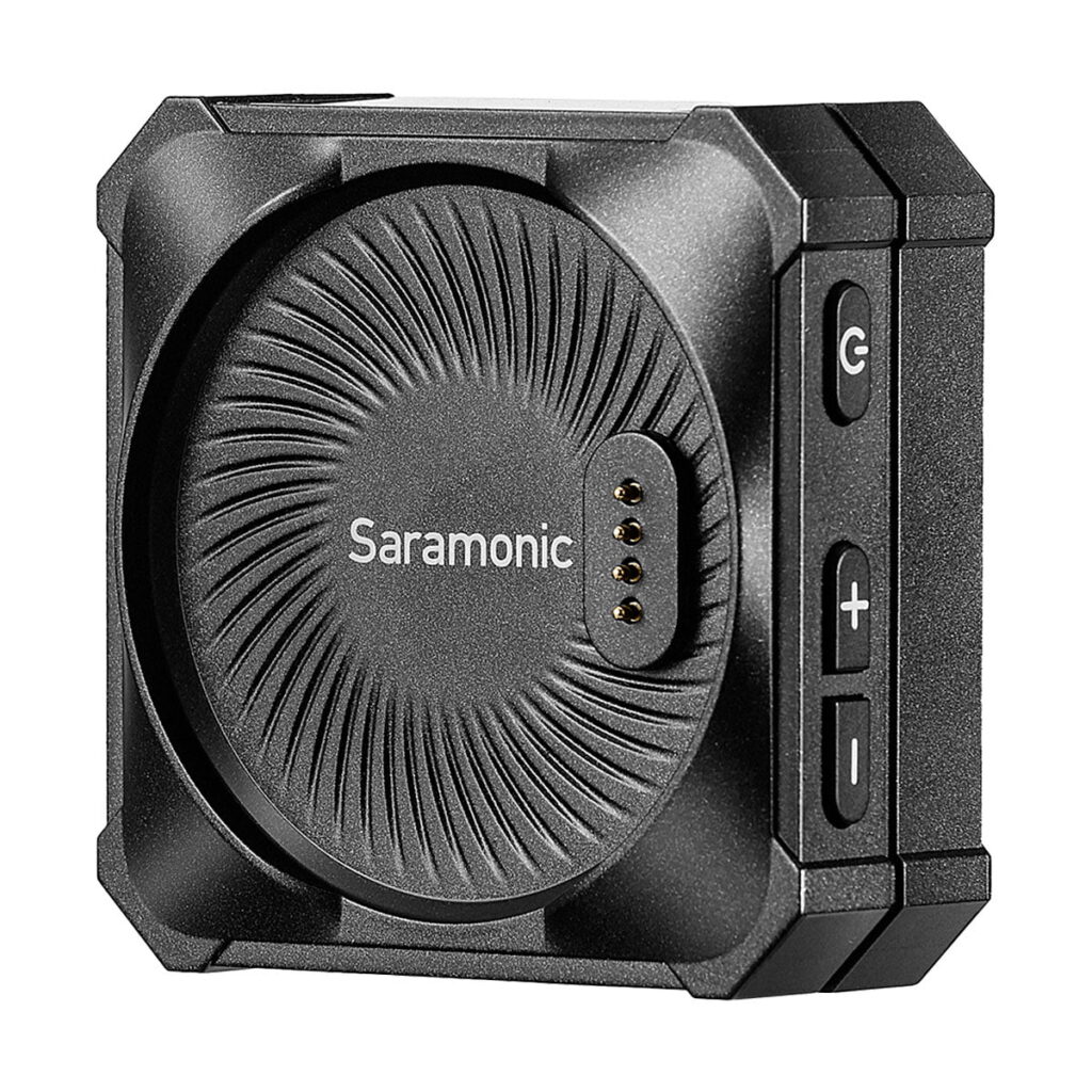Saramonic_Blink_ME_B2_005 Lähikuva Saramonic BlinkMe B2 -langaton mikrofonijärjestelmä, jossa on musta pyöreä kuvioitu pinta, neljä kultaista kosketintappia ja sivupainikkeet virran ja äänenvoimakkuuden säätöön.