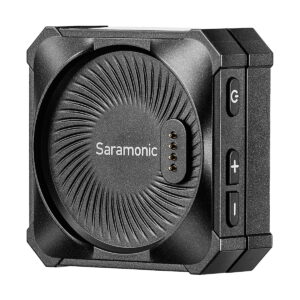 Saramonic_Blink_ME_B2_005 Lähikuva Saramonic BlinkMe B2 -langaton mikrofonijärjestelmä, jossa on musta pyöreä kuvioitu pinta, neljä kultaista kosketintappia ja sivupainikkeet virran ja äänenvoimakkuuden säätöön.