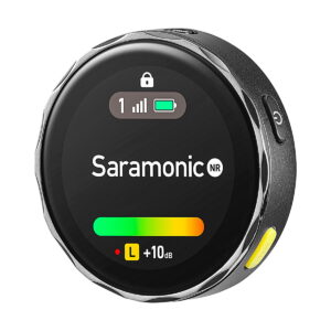 Saramonic_Blink_ME_B2_010 Lähikuva pyöreästä Saramonic BlinkMe B2 -langaton mikrofonijärjestelmä-lähettimestä, jossa on digitaalinen näyttö, jossa näkyy signaalin voimakkuus, akku ja äänenvoimakkuus sekä mustat, hopeiset ja keltaiset painikkeet.