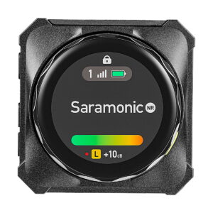 Saramonic_Blink_ME_B2_014 Lähikuva Saramonic BlinkMe B2 -langaton mikrofonijärjestelmä-lähettimestä, jossa on digitaalinen näyttö, jossa näkyy signaalin voimakkuus, pariston tila, lukituskuvake ja +10 dB:n äänitasomittari, jossa on vihreä ja keltainen palkki.