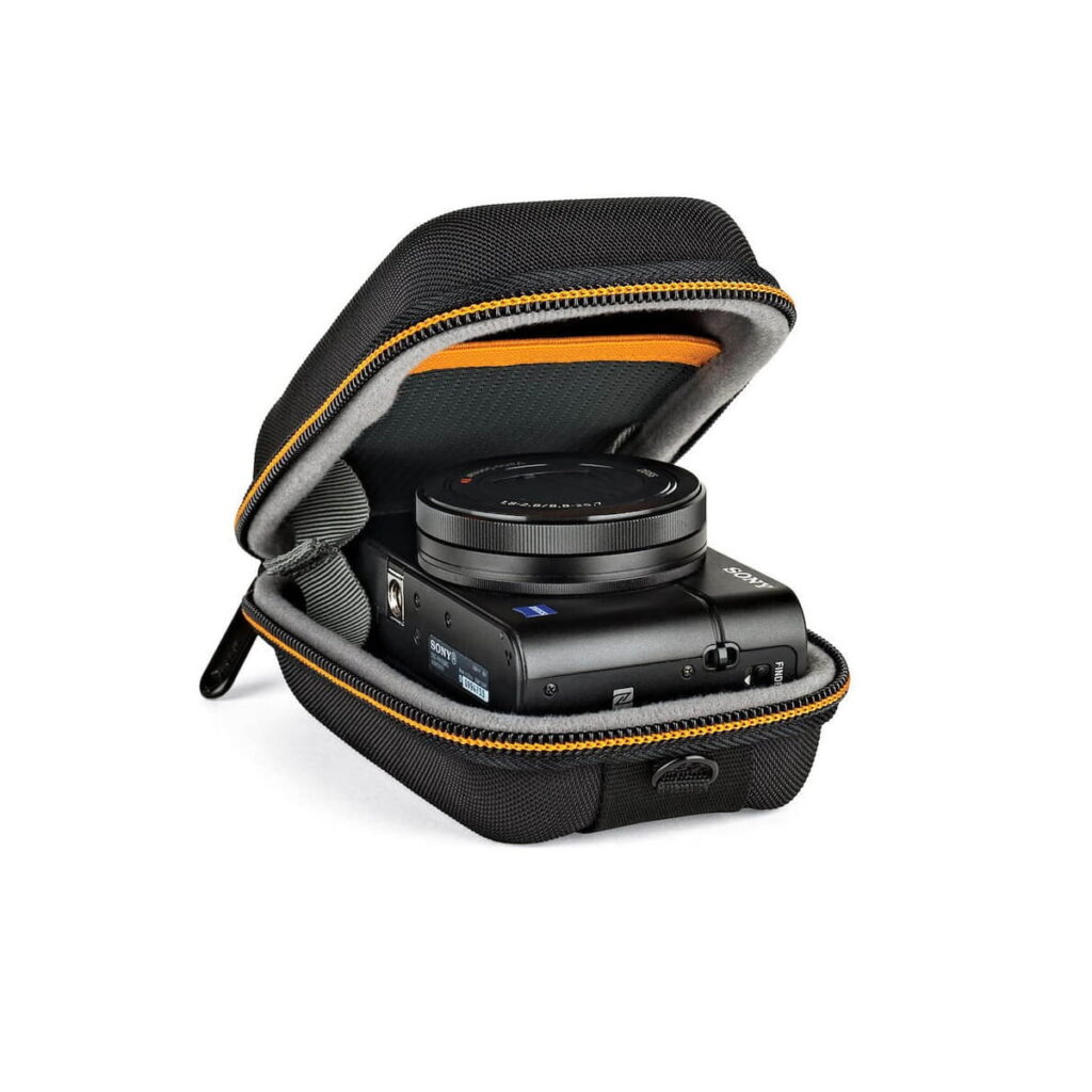 hardside_cs_20_01 Lowepro Hardside CS 20, musta vetoketjullinen suojakotelo, jossa on oranssi sisustus, pitää sisällään kompaktin mustan digitaalikameran, ja se on avattuna valkoista taustaa vasten.