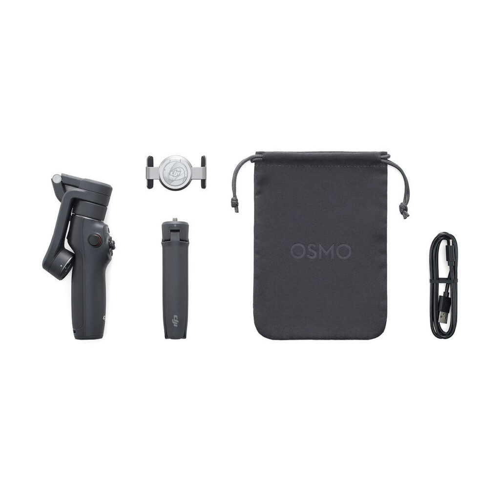 DJI_Osmo_Mobile_6_002 DJI Osmo Mobile 6 -gimbaali kännykälle -pakkaus sisältää mustan taitetun gimbaalin, jalustakiinnityksen, puhelimen pidikkeen, OSMO-merkityn kiristysnauhapussin ja USB-latauskaapelin, jotka kaikki näkyvät valkoisella pohjalla.