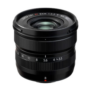 Fujifilm_XF_8mm_f_3_5_R_WR_001 Musta Fujifilm Fujinon XF 8mm f/3.5 R WR -objektiivi, jossa on kuvioidut tarkennusrenkaat ja aukkorenkaat, aukkoasteikko ja leveä etuelementti, on kuvattu valkoista taustaa vasten.