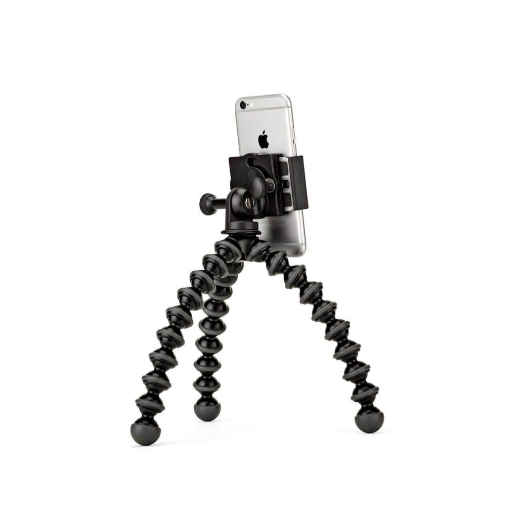 JOBY GripTight GorillaPod Stand PRO6 JOBY GripTight GorillaPod Stand PRO Jalusta Puhelimelle, joustava musta kolmijalka, jossa on puristinkiinnike, pitää älypuhelimen turvallisesti pystyssä valkoista taustaa vasten.