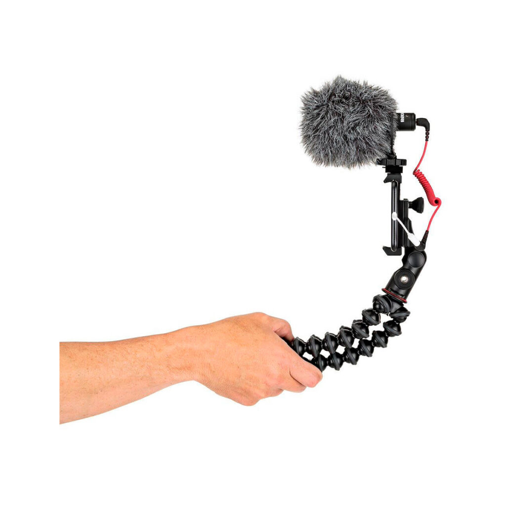 JOBY GripTight PRO 2 GorillaPod12 Käsi pitää JOBY GripTight PRO 2 GorillaPod Jalustakit Puhelimelle kameran ja ulkoisen mikrofonin (karvaisella tuulisuojalla) kanssa valkoista taustaa vasten.
