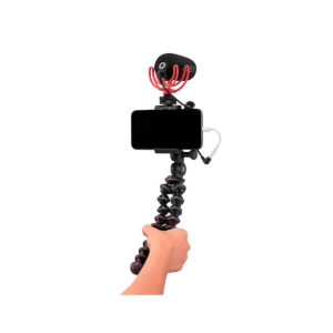 JOBY GripTight PRO 2 GorillaPod9 Käsi pitää JOBY GripTight PRO 2 GorillaPod -jalustaa älypuhelimille, johon on kiinnitetty puhelin, ulkoinen mikrofoni ja kaapeli, valmiina mobiilitallennukseen tai vloggaukseen valkoisella taustalla.