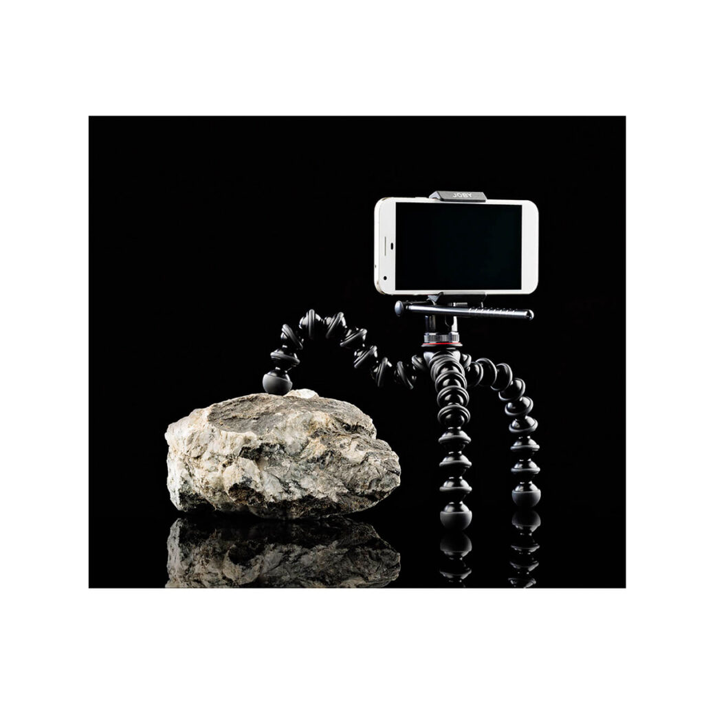 JOBY GripTight Pro Video GP2 JOBY GripTight Pro Video GP Jalusta Puhelimelle on asennettu heijastavalle mustalle pinnalle, ja yksi joustava jalustan jalka tarttuu suureen kiveen vakauden takaamiseksi täysin mustaa taustaa vasten.