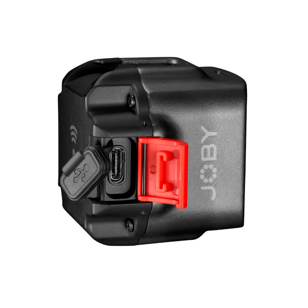 Pienikokoinen musta Joby Beamo - LED-valo, jossa on JOBY-logo, punainen salpa ja avoin kumikansi, joka paljastaa sivussa olevan USB-C-portin. Tausta on valkoinen.
