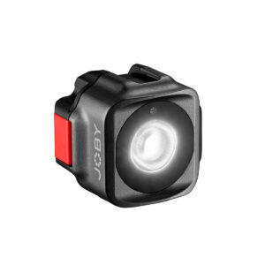 Joby-Beamo-Mini Pienikokoinen, musta, kuution muotoinen Joby Beamo Mini - LED-valo, jossa on punainen sivupainike ja pyöreä valaistu etuosa, kuvassa valkoisella pohjalla.