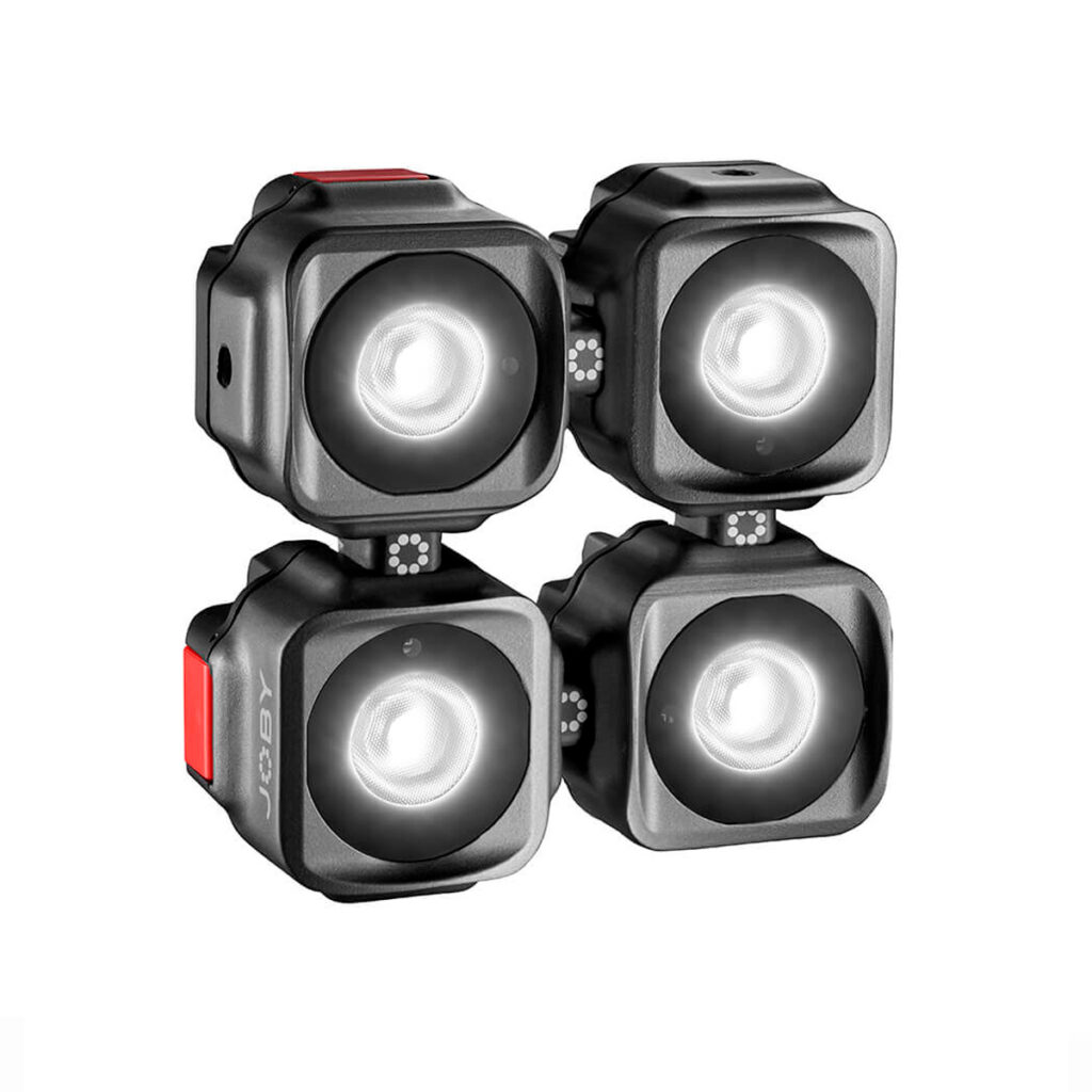 Neljä Joby Beamo Mini LED-valoa, jotka ovat kompakteja ja neliönmuotoisia ja joissa on pyöristetyt reunat, on sijoitettu 2x2-ruudukkoon; jokaisessa on hehkuva pyöreä keskus ja pieni punainen painike sivulla.