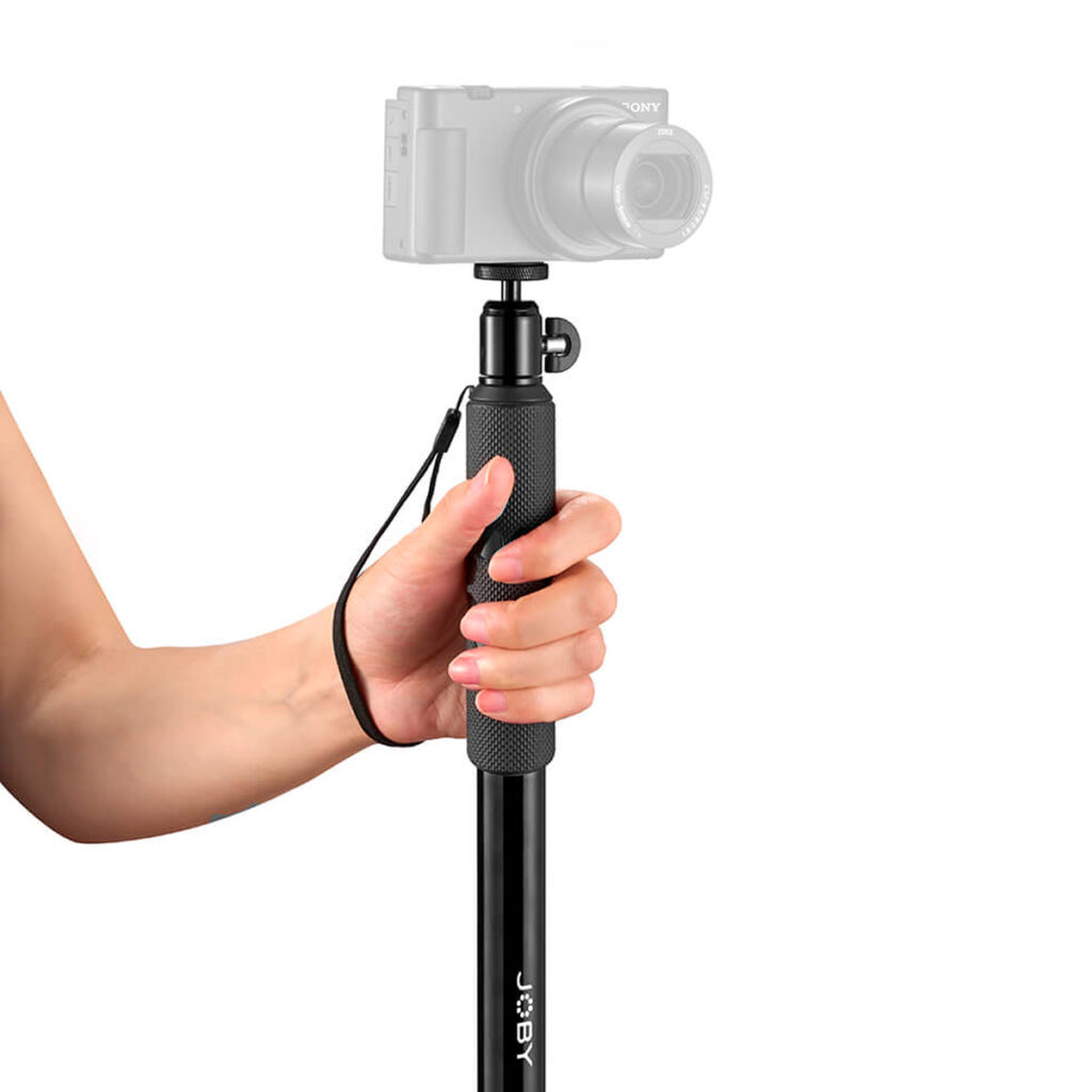 Joby-Compact-2in1-Monopod-4 Henkilö, jolla on Joby Compact 2in1 Monopod, jossa on kuvioitu kahva ja rannehihna, ja digitaalinen kamera kiinnitettynä sen päälle.