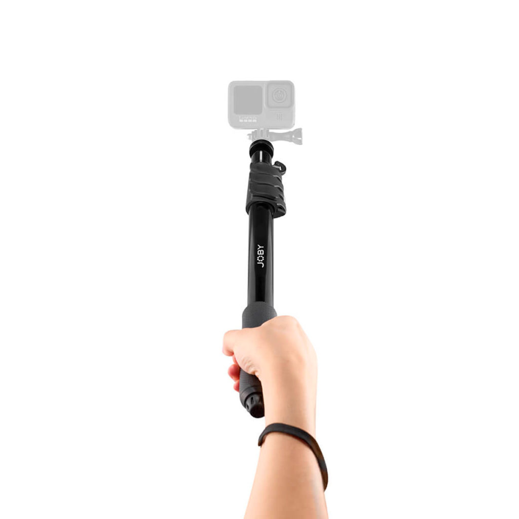 Joby-Compact-2in1-Monopod-5 Käsi pitää mustaa Joby Compact 2in1 -monopodia, joka on ojennettu ylöspäin, ja sen päälle on kiinnitetty epätarkka toimintakamera, joka on asetettu valkoista taustaa vasten.