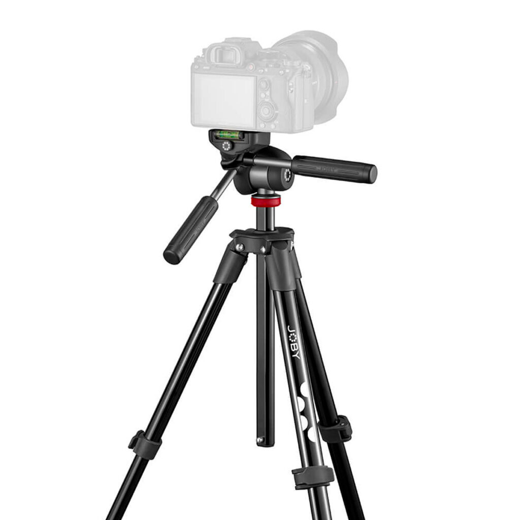 Joby-Compact-Advanced-3 Mustaa Joby Compact Advanced -kolmijalkaa, jossa on säädettävät jalat, panoraamakahva ja päälle asennettu kamera, esitellään valkoista taustaa vasten.