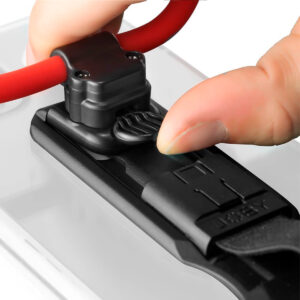 Joby-FreeHold-Universal-Kit-7 Lähikuva kädestä, joka säätää Joby FreeHold Universal Kitin mustaa puristinta ja kiinnittää punaisen hihnan valkoiseen pintaan.