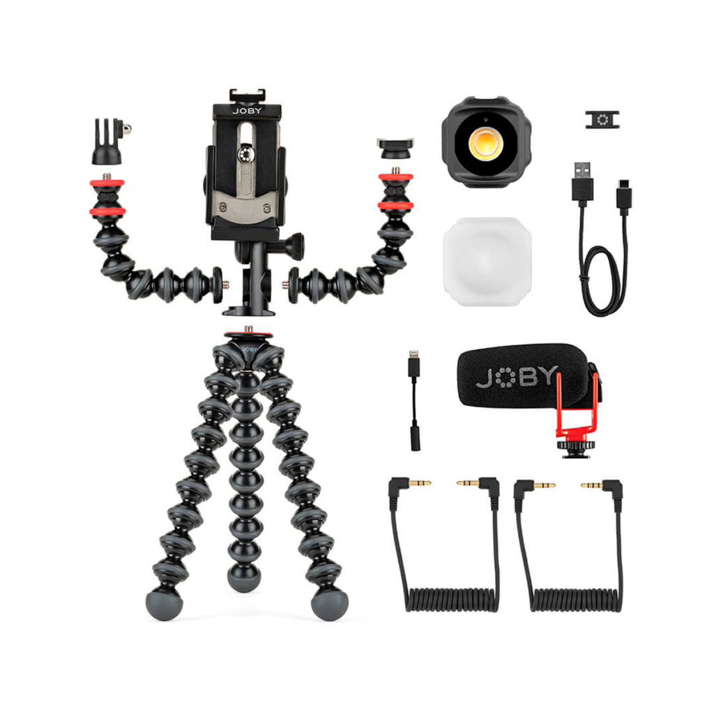 Joby-GorillaPod-Advanced-Mobile-Vlogging-Kit Joby GorillaPod Advanced Mobile Vlogging Kit, jossa on joustava musta jalusta, puhelimen kiinnike, irrotettavat varret, LED-valo diffuusorilla, USB-kaapeli, mikrofoni, punainen puhelimen pidike ja kaksi kierrettyä äänikaapelia valkoisella pohjalla.