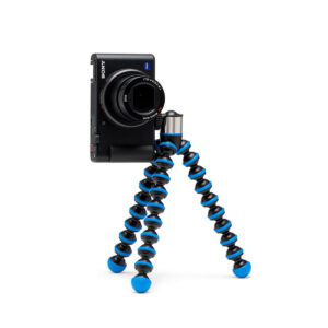 Joby-GorillaPod-Go-500-+-GripTight-360-Tripod-Kit-Blue-3 Kompakti Sony-kamera on kiinnitetty Joby GorillaPod Go 500 + GripTight 360 Tripod Kit Blue -jalustaan, jossa on mustat ja siniset segmentoidut jalat ja joka seisoo pystyssä valkoisella taustalla.
