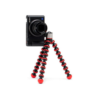 Joby-GorillaPod-Go-500-+-GripTight-360-Tripod-Kit-Red-2 Joby GorillaPod Go 500 + GripTight 360 Tripod Kit Red tukee mustaa digitaalikameraa, ja sen joustavat punaiset ja mustat segmenttijalat on sijoitettu valkoista taustaa vasten.