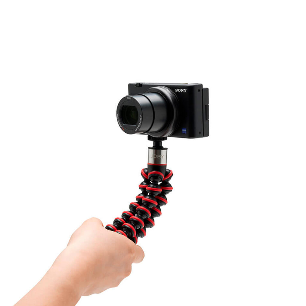 Joby-GorillaPod-Go-500-+-GripTight-360-Tripod-Kit-Red-3 Käsi pitää Joby GorillaPod Go 500 + GripTight 360 Tripod Kit Red -jalustaa, johon on kiinnitetty Sony-kompaktikamera, valkoista taustaa vasten.