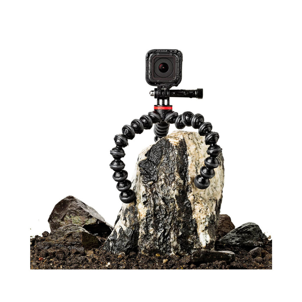 Joby Gorillapod 500 Action7 JOBY GorillaPod 500 Action Jalusta Musta/Harmaa, jonka joustavat jalat kietoutuvat tukevasti kiven ympärille, tukee kompaktia kameraa maaperän ja pienempien kivien keskellä.