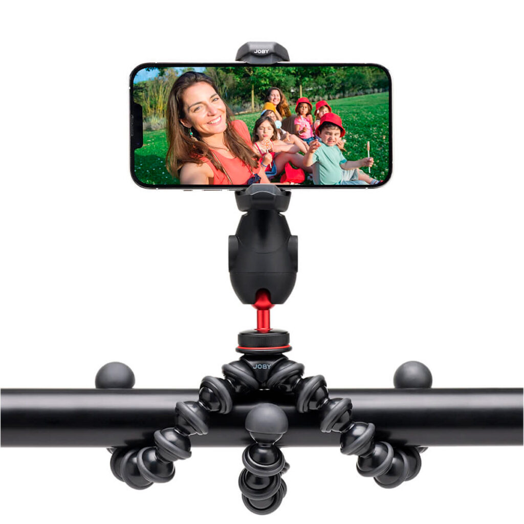 Ryhmäselfie otetaan ulkona vihreällä nurmikolla älypuhelimella, joka on kiinnitetty vaakatolppaan Joby GripTight Pro 3 Kit - puhelinjalusta, joka on asennettu joustavasti.