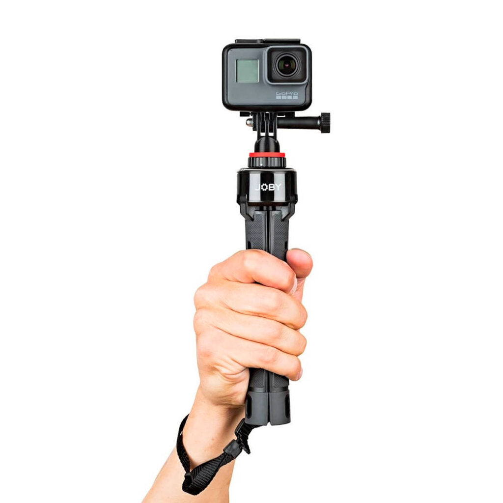 Joby-GripTight-Pro-TelePod-4 Käsi pitää Joby GripTight Pro TelePodia, johon on kiinnitetty GoPro-toimintakamera valkoista taustaa vasten.