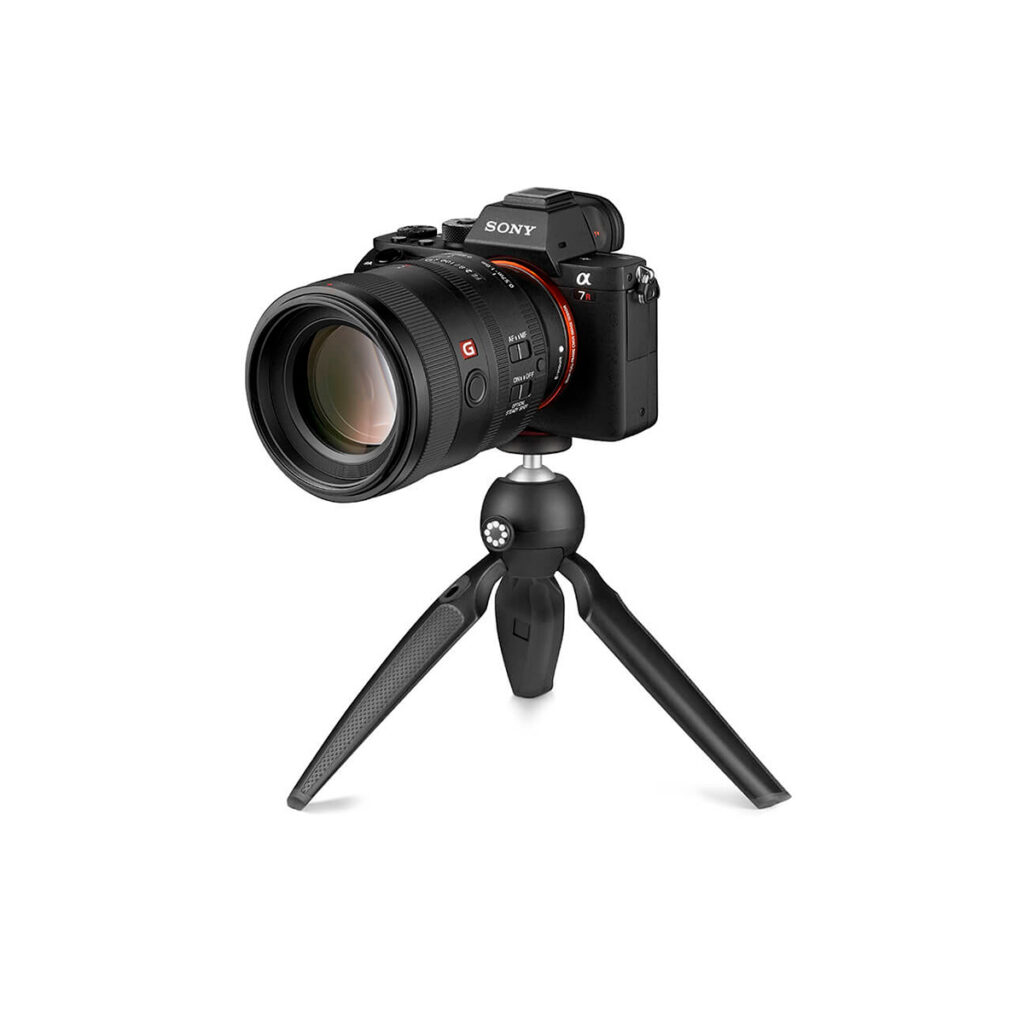 Joby HandyPod5 Musta Sony-digitaalikamera, jossa on suuri objektiivi, on kiinnitetty JOBY HandyPod Jalusta Musta -nimiseen kompaktiin mustaan kolmijalkaan valkoista taustaa vasten.