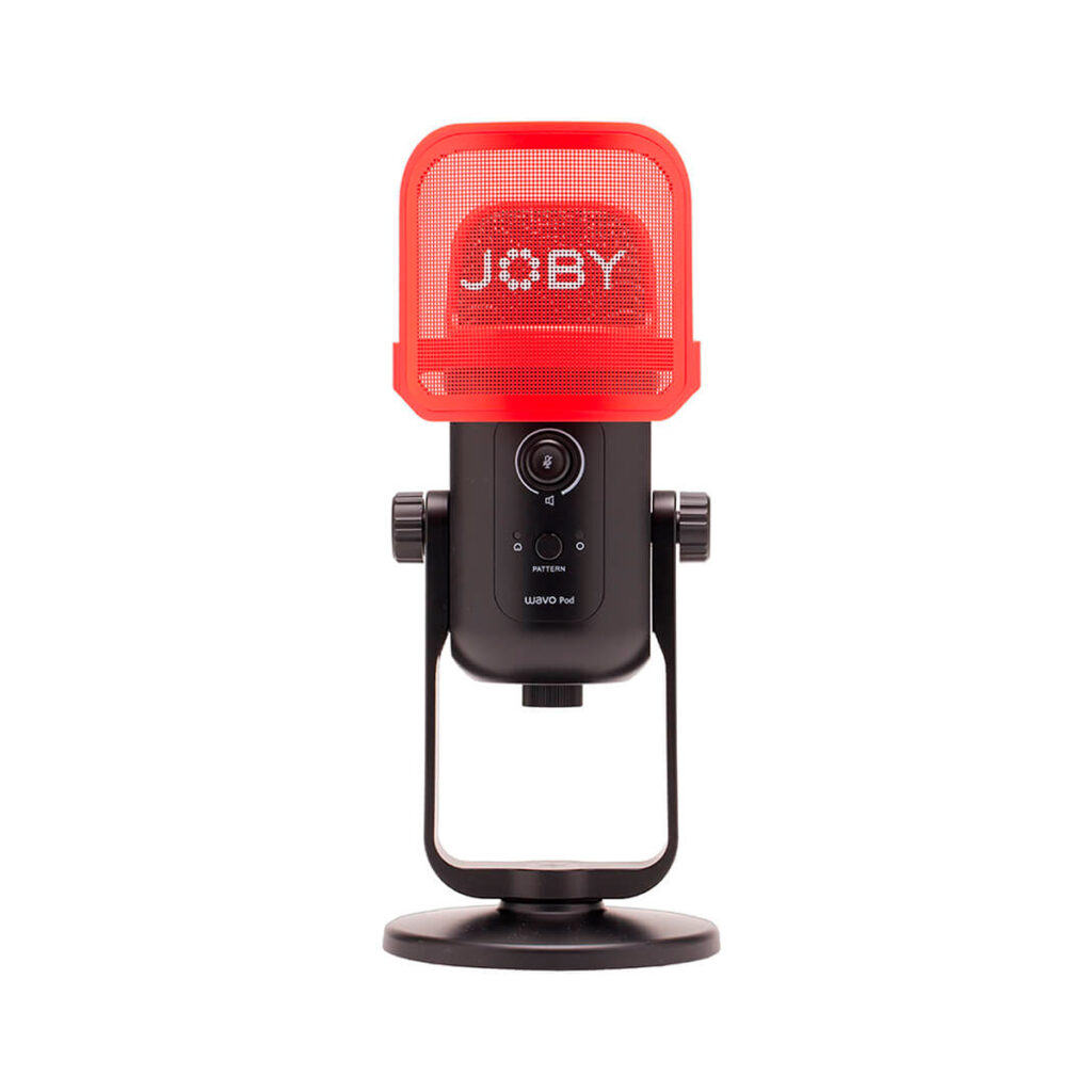 Joby-Microphone-Wavo-POD Joby Wavo POD -mikrofoni on musta pöytämikrofoni, jossa on JOBY-logolla varustettu punainen verkkomallinen pop-suodatin, joka on asennettu pyöreään jalustaan valkoista taustaa vasten.