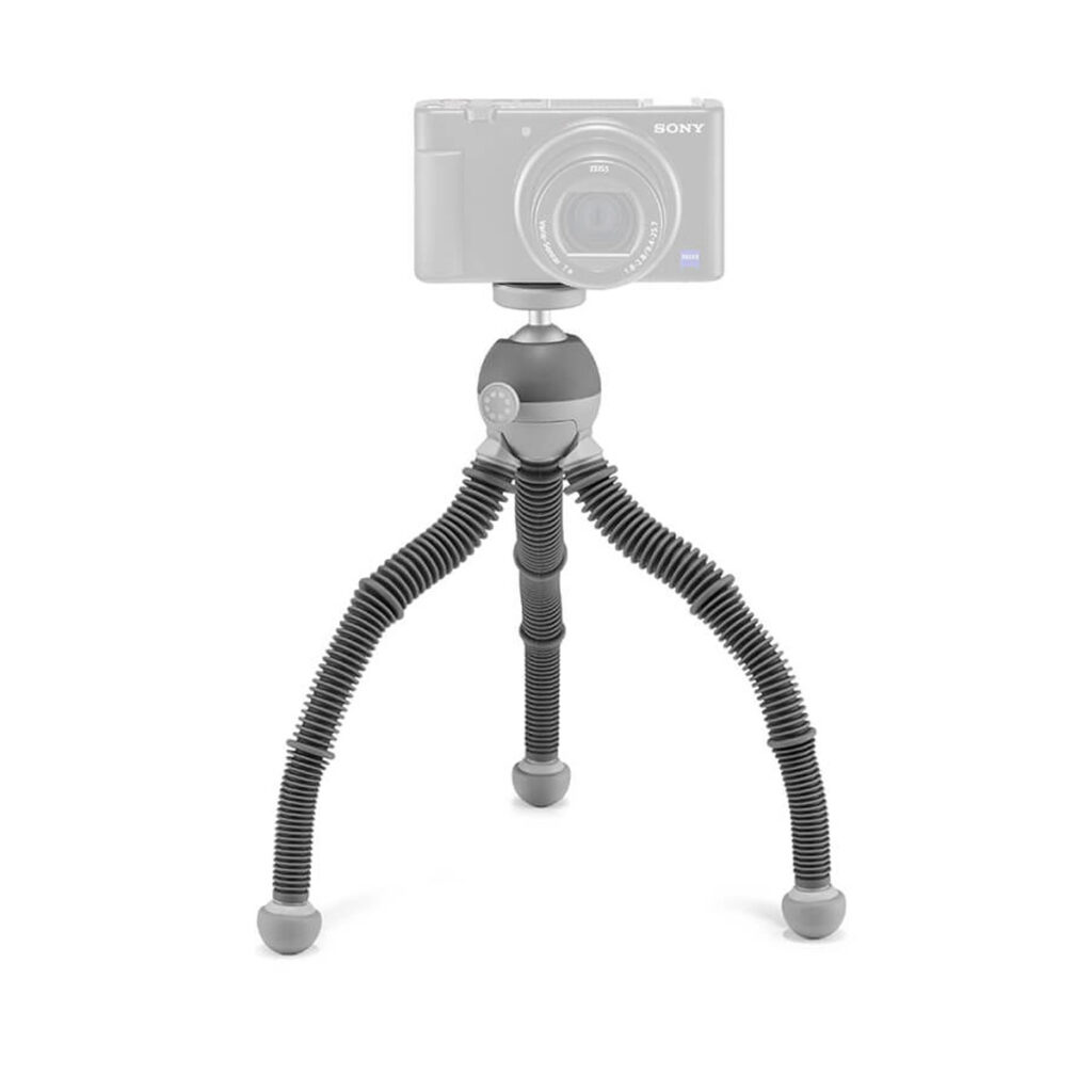 Joby PodZilla Flexible Tripod Kit M Harmaa sisältää taipuisat jalat ja kumijalat, jotka pitävät turvallisesti pienen digitaalikameran (kamera on kuvassa haalistuneena korostamassa jalustaa).