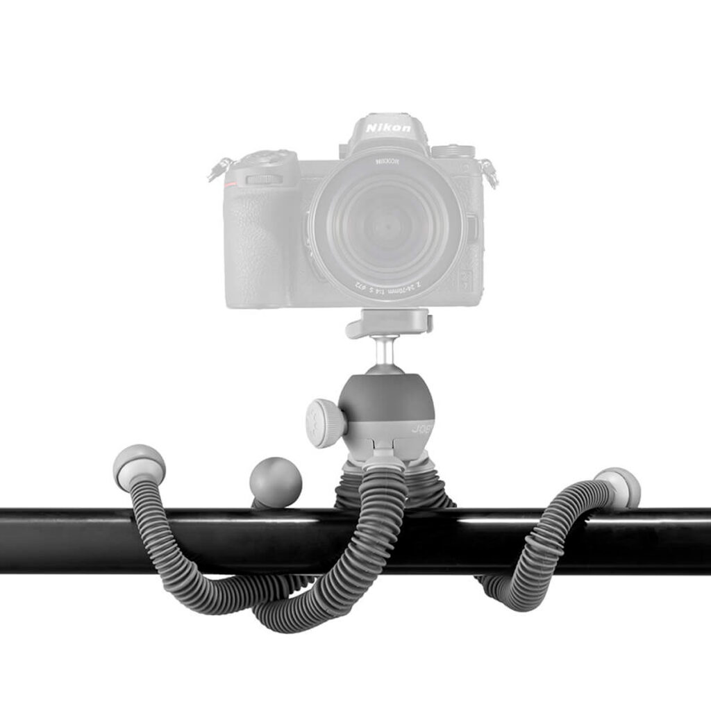 Taivutettavilla jaloilla varustettu Joby PodZilla Flexible Tripod Large on kiedottu vaakasuoran mustan tangon ympärille, ja se pitää kameraa turvallisesti sen säädettävän kuulapääkiinnikkeen avulla valkoista taustaa vasten.
