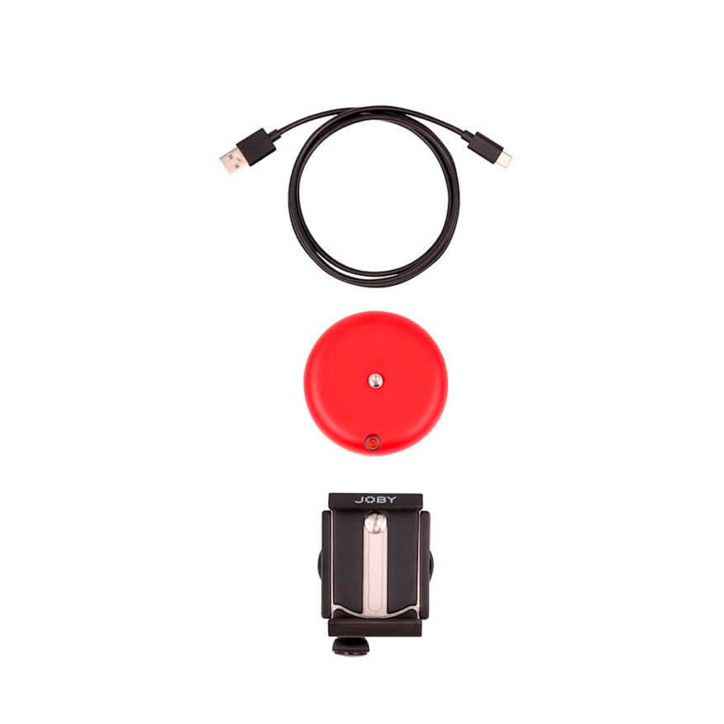 Joby-Spin-Phone-Mount-Kit-2 Joby Spin Phone Mount Kit, joka sisältää mustan JOBY-puhelinpidikkeen, mustan USB-kaapelin ja punaisen pyöreän laitteen, jossa on pieni painike, on sijoitettu pystysuoraan valkoiselle taustalle.