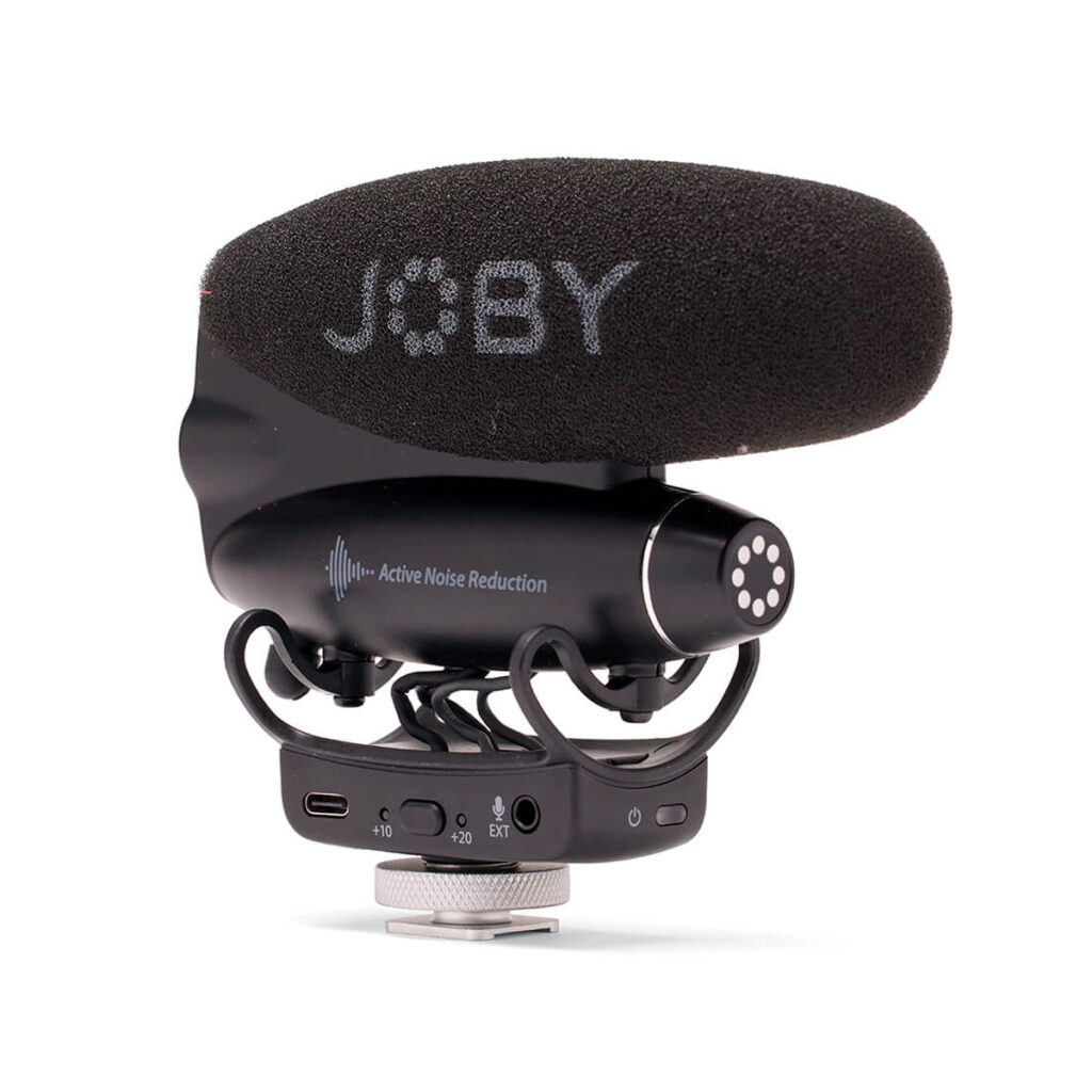 Joby-Wavo-Pro Musta Joby Wavo Pro - Mikrofoni, jossa on vaahtomuovinen tuulisuoja ja JOBY-brändi, ja jossa on melunvaimennustarra, ohjauspainikkeet ja portit rungossaan, on kiinnitetty kameran kenkäadapteriin.
