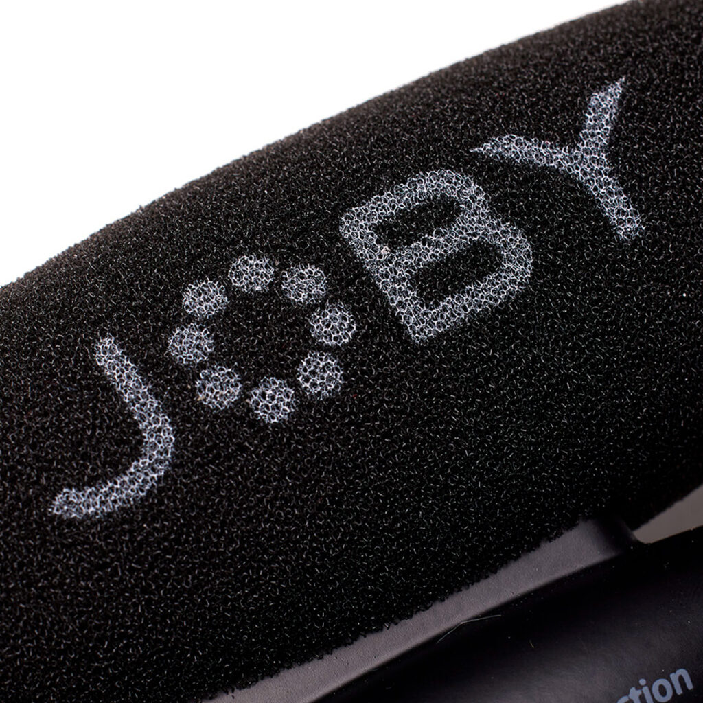 Joby-Wavo-Pro-6 Lähikuva mustasta vaahtomuovisesta tuulisuojasta, jossa on valkoisilla kuvioiduilla kirjaimilla "JOBY", osa Joby Wavo Pro - Mikrofoni audio mikrofonin lisävarustetta.