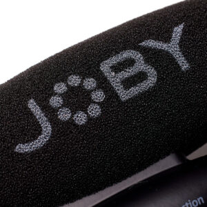 Joby-Wavo-Pro-6 Lähikuva mustasta vaahtomuovisesta tuulisuojasta, jossa on valkoisilla kuvioiduilla kirjaimilla "JOBY", osa Joby Wavo Pro - Mikrofoni audio mikrofonin lisävarustetta.