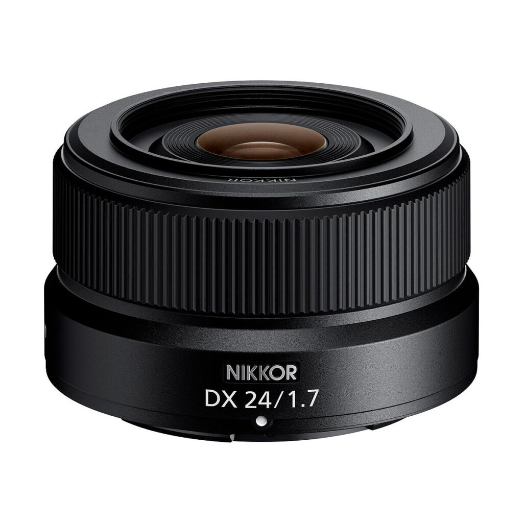 Nikon_Nikkor_Z_DX_24mm_f_1_7_001 Musta Nikon Nikkor Z DX 24mm f/1.7 -objektiivi näkyy valkoisella pohjalla korostaen sen kompaktia muotoilua ja yksityiskohtaista kuvioitua tarkennusrengasta.