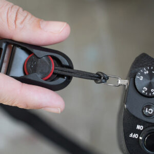 Käsi kiinnittää Peak Design Anchor Connector 4-Pack Black -liittimen DSLR-kameran hihnasilmukkaan, ja kameran säätöpyörässä on ON- ja OFF-merkinnät.