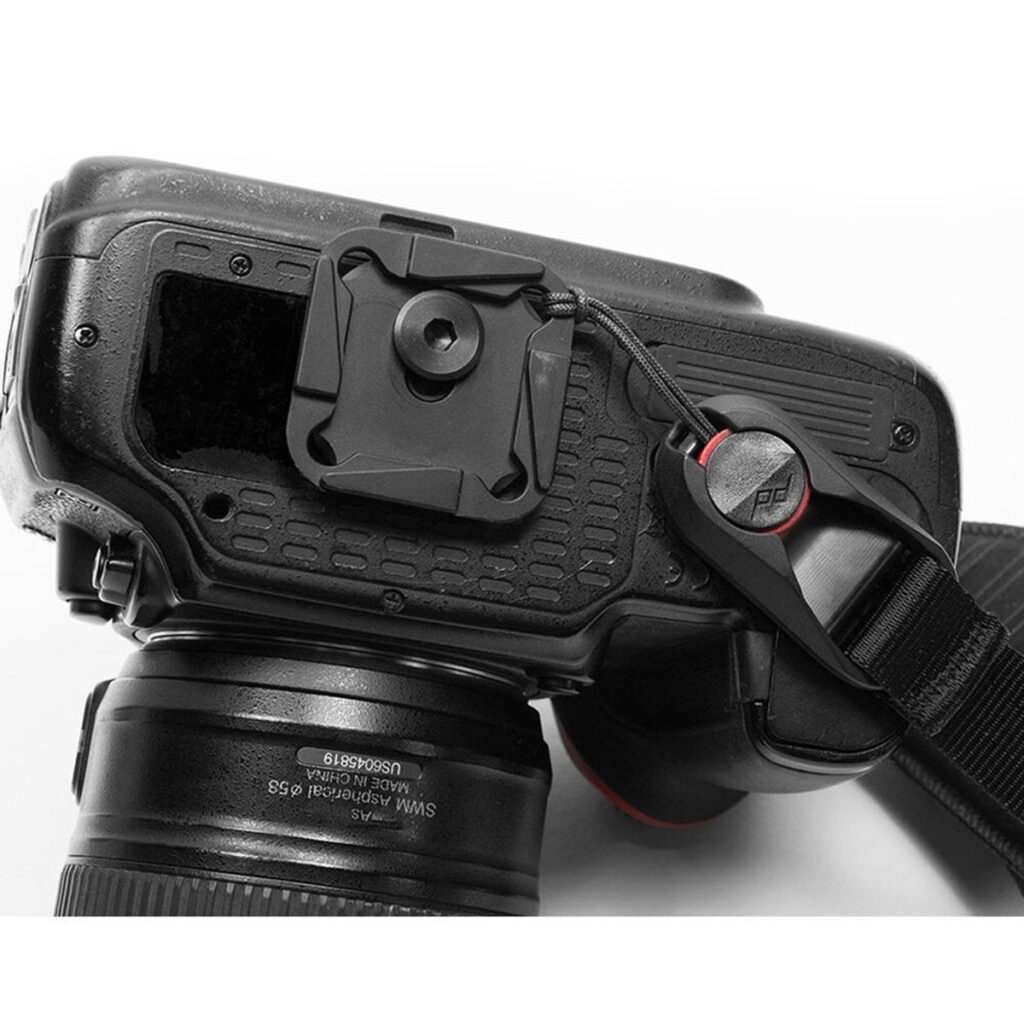 Peak-Design-Clutch-3 Lähikuva DSLR-kameran takaosasta ja sivusta, jossa on objektiivi, pikakiinnityslevy alla ja musta Peak Design Clutch -rannehihna kiinnitettynä ankkurilinkillä.