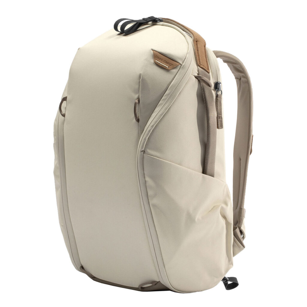 Peak-Design-Everyday-Backpack-Zip-15L-bone-1 Peak Design Everyday Backpack Zip 15L -kamerareppu, väri Bone, sisältää virtaviivaisen beigen muotoilun, useita ulkotaskuja, yläkahvan, pehmustetut olkahihnat ja ruskeat nahkakoristeet.