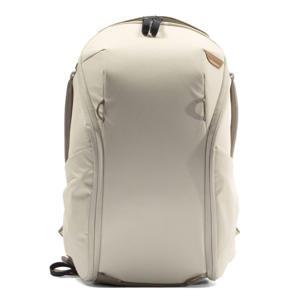 Peak-Design-Everyday-Backpack-Zip-15L-bone-2 Peak Design Everyday Backpack Zip 15L -kamerareppu Bone on pystyssä valkoista taustaa vasten, ja siinä on minimalistinen beige muotoilu, sivutaskut, yläkahva ja ruskeat koristeet.