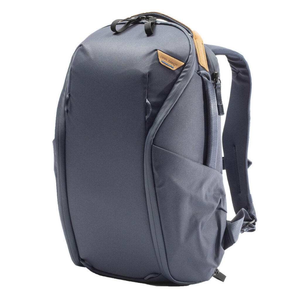 Peak-Design-Everyday-Backpack-Zip-15L-midnight-1 Peak Design Everyday Backpack Zip 15L Midnight on moderni, tummanharmaa reppu, jossa on tyylikäs muotoilu, pehmustetut olkahihnat, sivutaskut ja ruskehtava aksentti lähellä yläreunaa. Se seisoo pystyssä valkoista taustaa vasten.