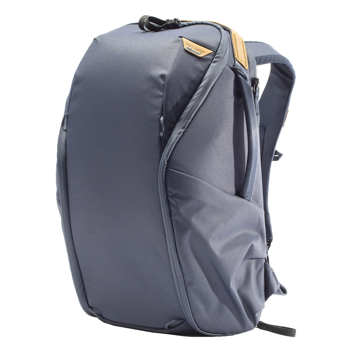 Peak Design Everyday Backpack Zip 20L -kamerareppu, tummansininen, sisältää pehmustetut olkahihnat, yläkahvan, sivutaskun ja ruskehtavan nahkaisen korostuksen vetoketjun kohdalla, ja se on kuvattu pystyasennossa valkoisella pohjalla.