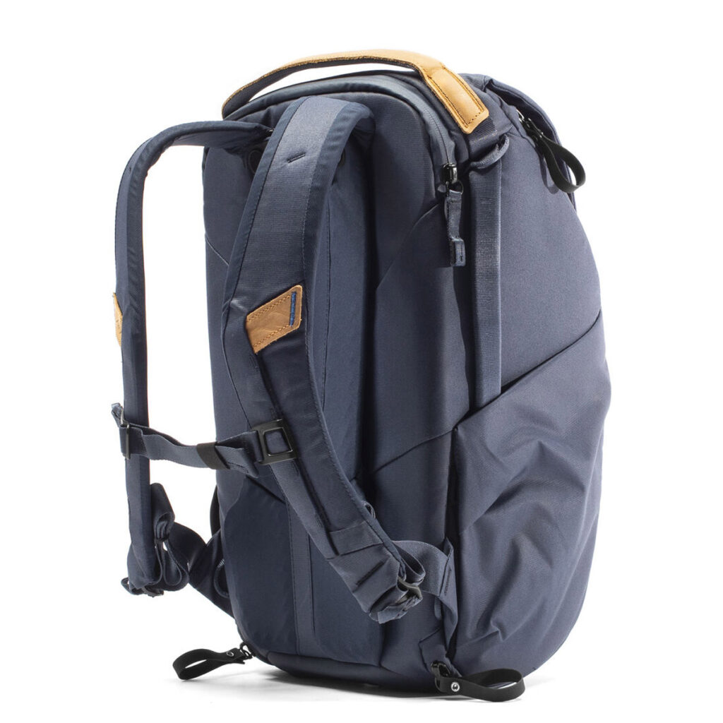 Peak-Design-Everyday-Backpack-v2-20l-midnight-3 Tummansinisessä Peak Design Everyday Backpack v2 20L -kamerareppu, jossa on ruskehtavat nahkakoristeet, pehmustetut olkahihnat, yläkahva ja vetoketjulliset lokerot, kuvassa pystyasennossa valkoisella pohjalla.