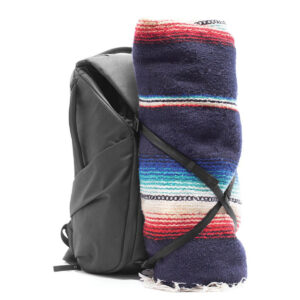 Peak-Design-Everyday-Backpack-v2-30l-black-08 Peak Design Everyday Backpack v2 30L -kamerareppu, musta, sisältää värikkään raidallisen huovan, joka on rullattu kokoon ja kiinnitetty sivulle mustilla hihnoilla, kuvassa valkoista taustaa vasten.