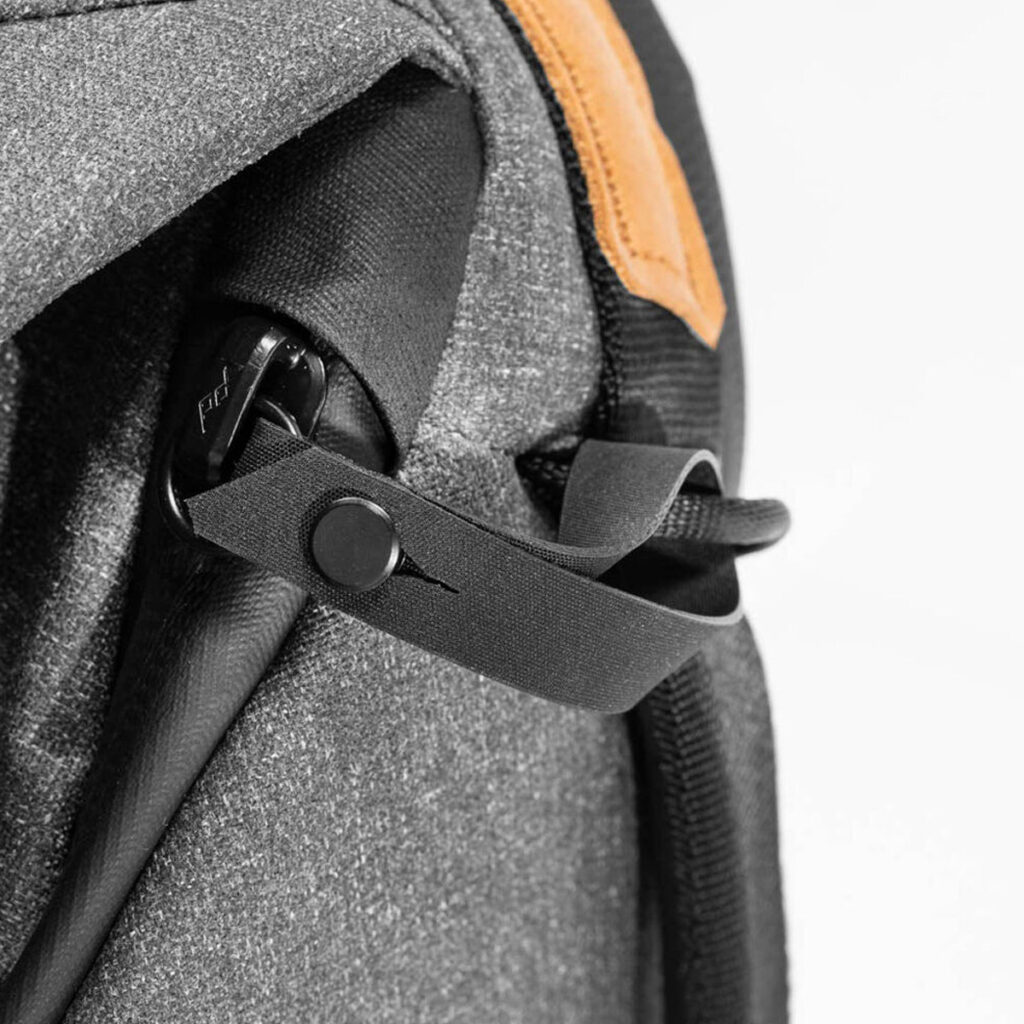 Peak-Design-Everyday-Backpack-v2-30l-charcoal-6 Lähikuva Peak Design Everyday Backpack v2 30L -repusta tummanharmaana, jossa on musta hihna nappikiinnityksellä ja pieni ruskehtava nahkainen korostus oikeassa yläkulmassa. Kuvioidut materiaalit näyttävät kestäviltä.