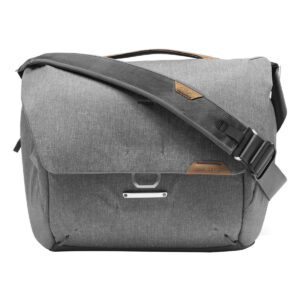 Peak-Design-Everyday-Messenger-13L-v2-Ash-2 Peak Design Everyday Messenger 13L V2 - Ash on harmaa laukku, jossa on suuri läppä, säädettävä olkahihna ja yläkahva. Laukussa on metalli- ja nahkakoristeita, ja se on ihanteellinen kannettavien tietokoneiden tai kameravarusteiden kuljettamiseen.