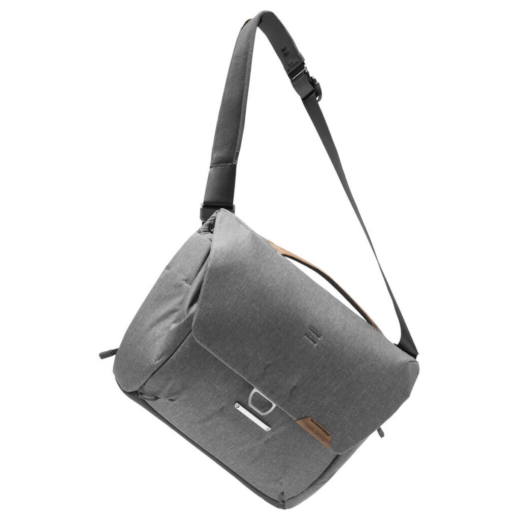 Peak-Design-Everyday-Messenger-13L-v2-Ash-3 Peak Design Everyday Messenger 13L V2 -laukussa Ash on harmaa muotoilu, jossa on pitkä säädettävä musta hihna, etuläppäsuljenta ja pieni ruskehtava korostus yläosan lähellä. Laukku näkyy valkoisella pohjalla.